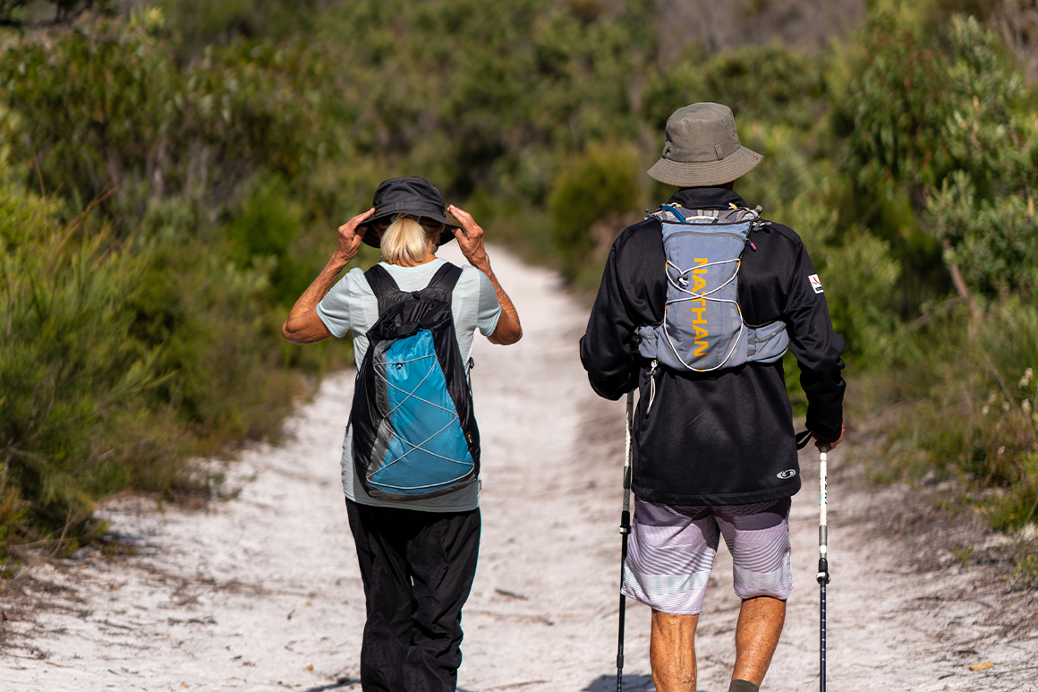 Man and woman hiker in loose clothing wearing hats and water bladder packs.