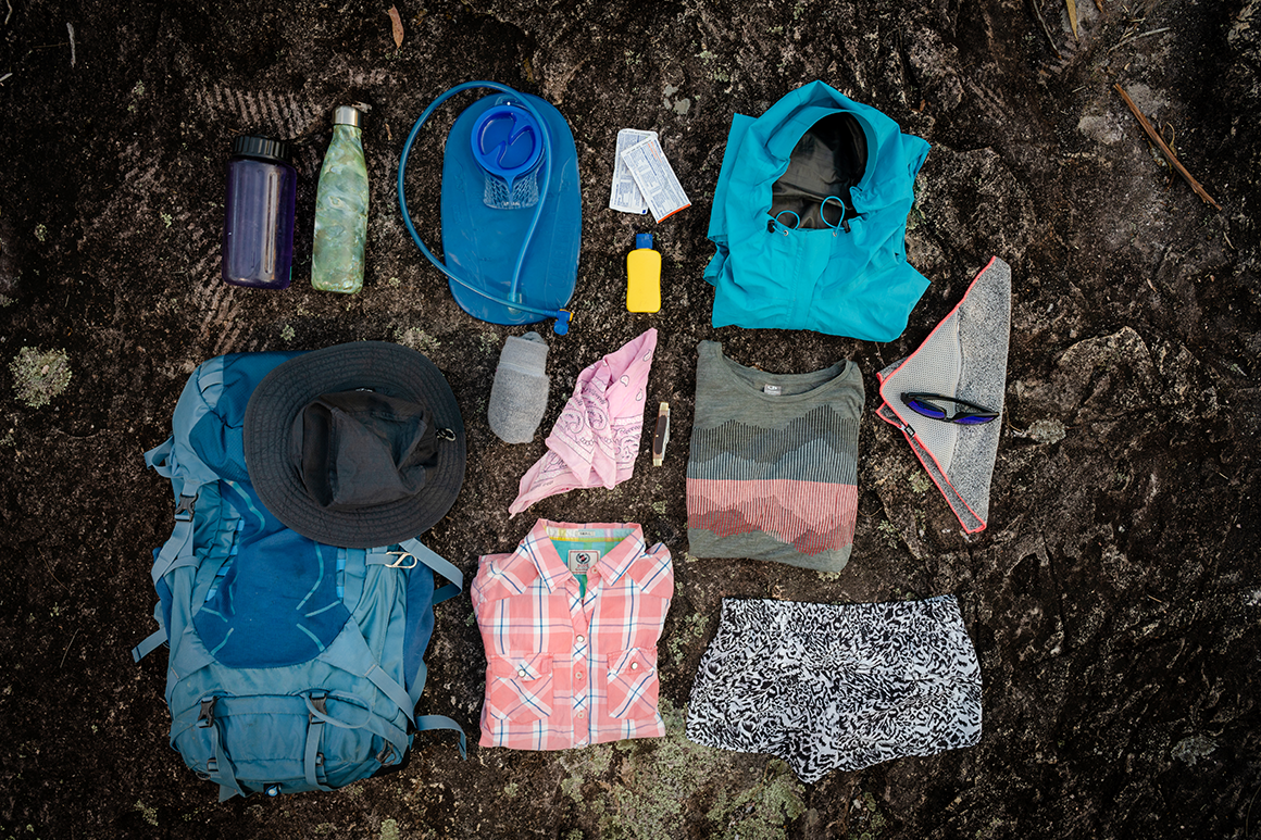 Hiking gear such as water bladder, bottle, bandana, sunscreen laid out on a rock.