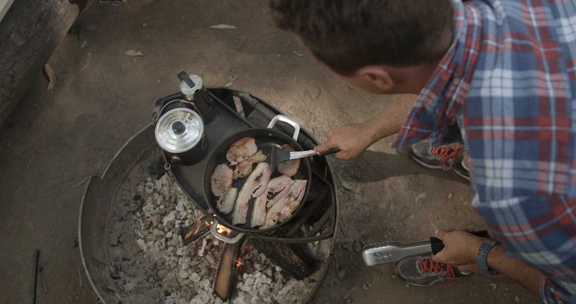 Man cooking up bacon on a small barbecue in D’Aguilar National Park
