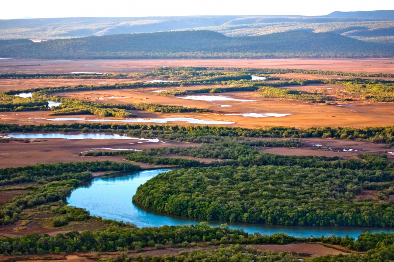 Aerial image of curving river and wetland plains with vegetated hills in background.